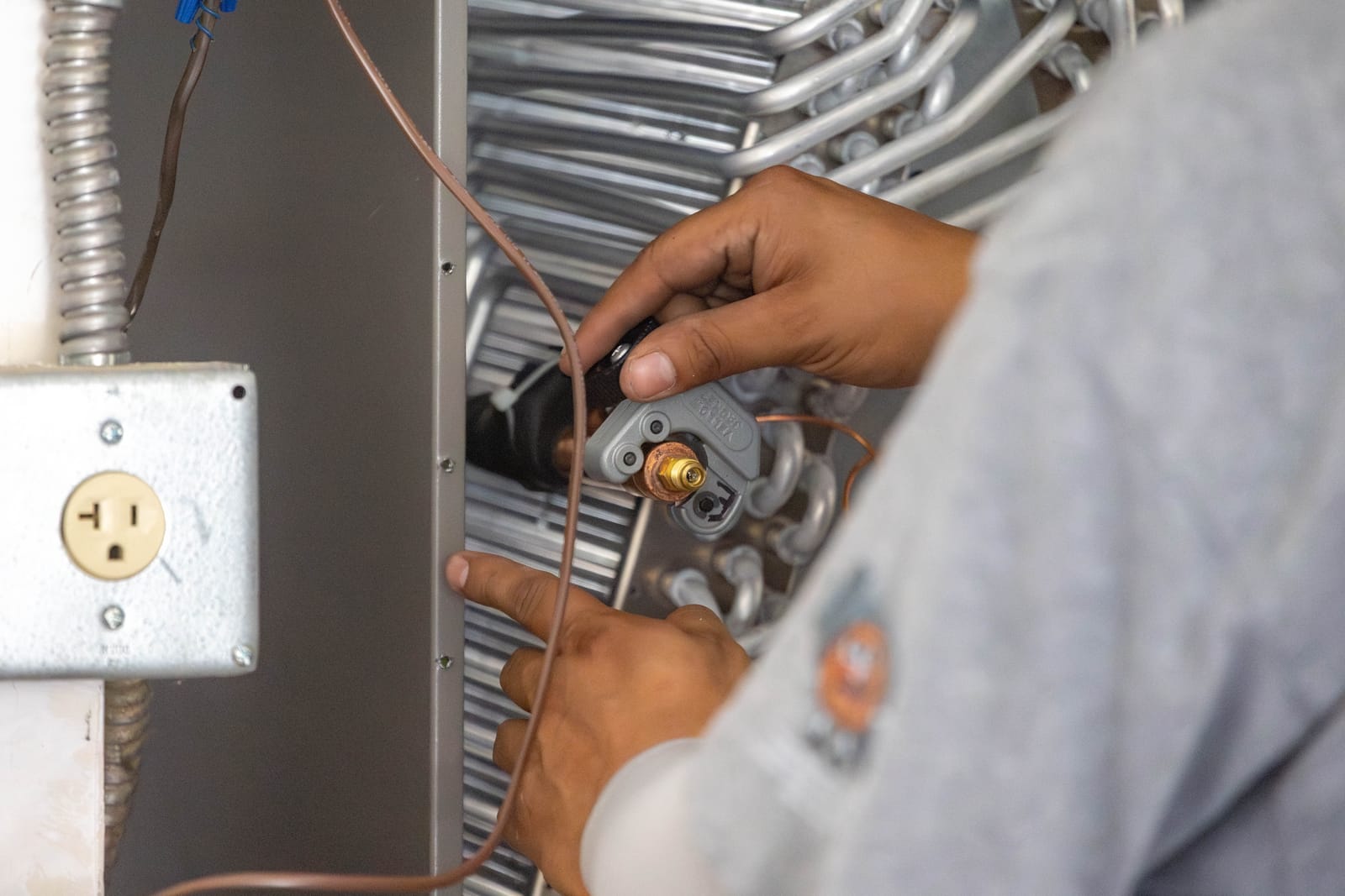 Close-up of an HVAC Ministries technician checking the refrigerant line on an evaporator coil during a maintenance tune-up
