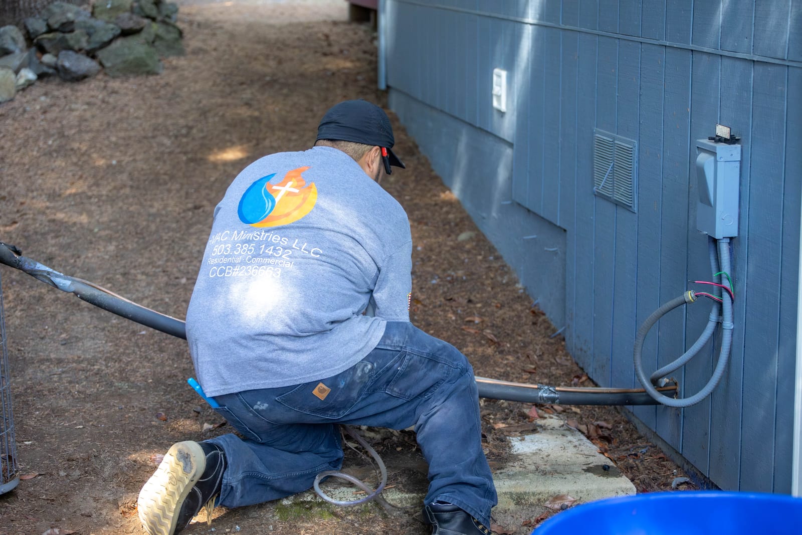 An HVAC Ministries technician in a branded company shirt servicing the exterior electrical disconnect beside a Salem-area home
